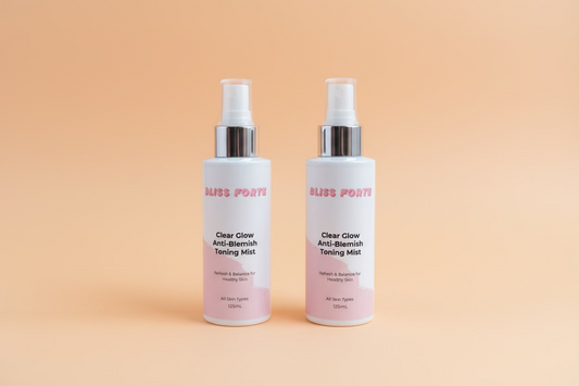 Two bottles of Bliss Forte Clear Glow Anti-Blemish Toning Mist on a green towel with a wooden background.