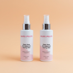 Two bottles of Bliss Forte Clear Glow Anti-Blemish Toning Mist on a green towel with a wooden background.