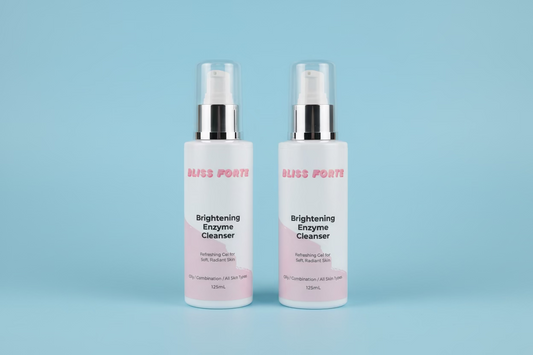 Two bottles of Bliss Forte Brightening Enzyme Cleanser on a green towel with a wooden background.